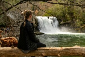 Une femme se ressource devant une cascade en pleine nature, symbole d’un accompagnement du burn-out en douceur.